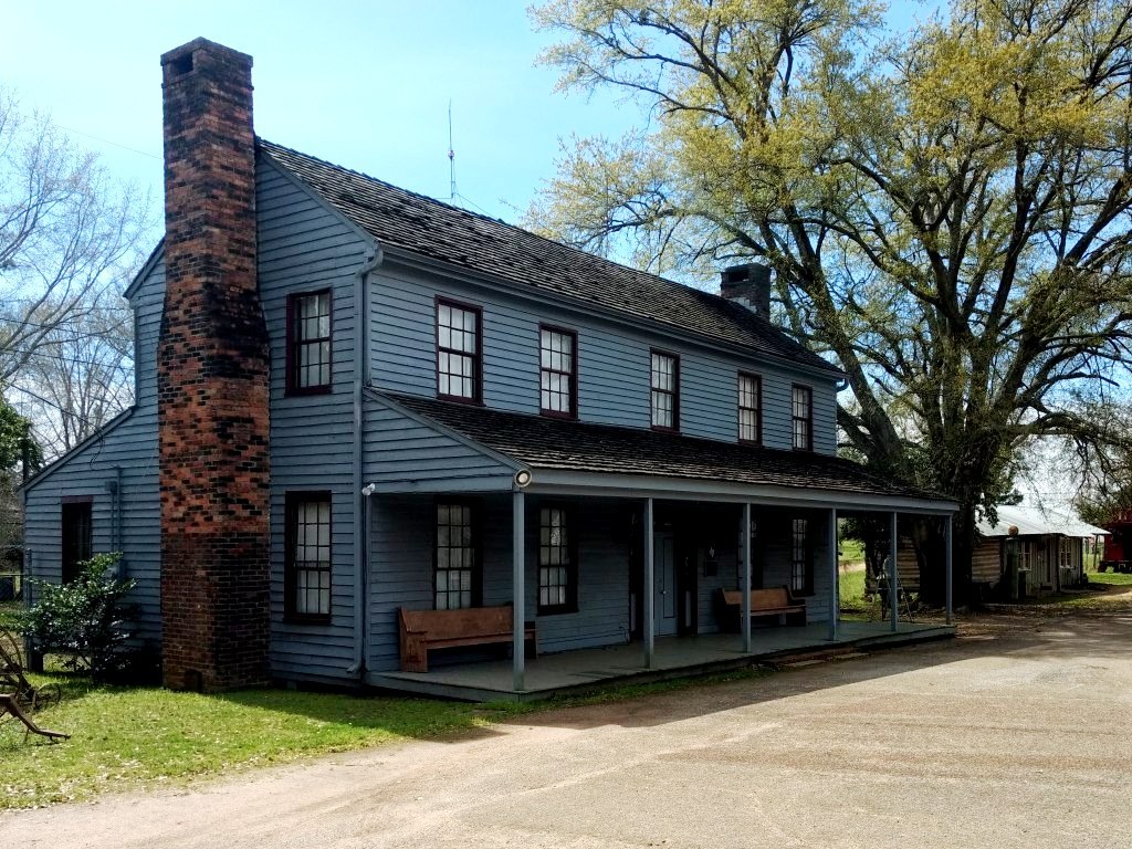 The Millard-Lee House: a two-story gray clapboard house with a tall brick chimney and a long front porch with benches.